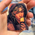 Hand holding a sticker with a stylized illustration of a character eating an popsicle