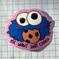 Sticker with a cartoon character and text 'Me want that cookie' on a grid background