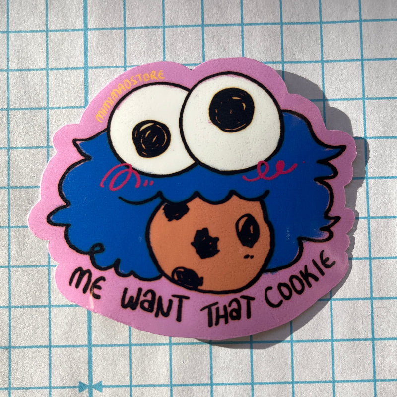 Sticker with a cartoon character and text 'Me want that cookie' on a grid background