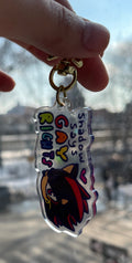 Hand holding a keychain with shadow hedgehog design and text in front of a blurred cityscape.