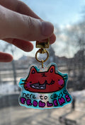 Keychain with cartoon character and text held in front of a cityscape