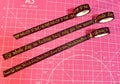 Three rolls of gold text tape on a pink cutting mat with grid lines.