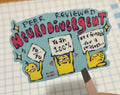 Hand holding a colorful sticker with cartoon characters on a piece of graph paper.